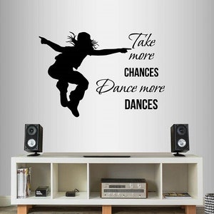 May include: Black and white silhouette of a dancer with the text "Take more chances, Dance more dances". The image is on a white wall above a white shelf with speakers and a stereo.