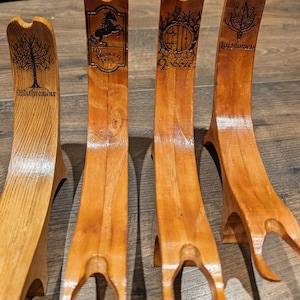 Puede incluir: Cuatro soportes de madera con un diseño curvo y una base en forma de horquilla. Cada soporte presenta un diseño y texto grabado diferente, incluyendo un árbol, un caballo, una puerta y hojas. La madera tiene un color marrón claro natural.