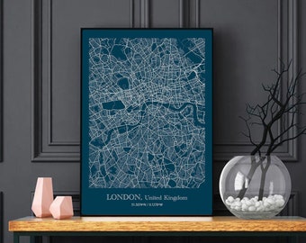 Può includere: Una stampa incorniciata nera di una mappa di Londra, Regno Unito, con linee bianche che mostrano le strade e le vie d'acqua. La stampa è appesa a un muro grigio scuro sopra un tavolo consolle in legno con una cornice in metallo nero. Un vaso di vetro trasparente con pietre bianche e un ramo secco è sul tavolo. Due oggetti decorativi rosa sono sul tavolo.