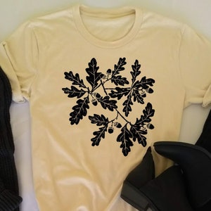 Puede incluir: Una camiseta de color crema suave con una silueta negra de una rama de roble con hojas y bellotas. El texto "Soft Cream" est&aacute; impreso en la esquina inferior izquierda de la camiseta. El texto "Gift Imagine Original" est&aacute; impreso debajo del texto "Soft Cream".