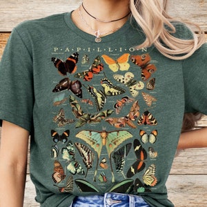 May include: A dark green t-shirt featuring a detailed illustration of various butterflies and moths. The word "PAPILLON" is printed at the top. The shirt is made of a soft material and has a classic crew neck.