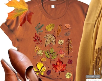 Puede incluir: Una camiseta marrón con un gráfico de diferentes tipos de hojas y sus nombres, incluyendo 'Jew', 'Elder', 'Sycamore', 'Rowan', 'Turkey Oak', 'Sweet Chestnut', 'Birch', 'Beech', 'Maple', 'Oak', 'Willow', 'Ash', 'Elm', 'Hawthorn', 'Horse Chestnut', 'Lime', 'Redwood', 'Spindle', 'Yew', 'Holly', 'Ivy', 'y 'get fugue - original Autumn'.