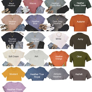 Puede incluir: Una colecci&oacute;n de 16 camisetas de diferentes colores con varias descripciones de texto, incluyendo "Black Heather", "Mauve", "Heather Dusty Blue", "Heather Forest Green", "Heather Peach", "Heather Blue", "Dark Grey Heather", "Autumn", "Heather Midnight Navy", "Heather Ice Blue", "White", "Army", "Soft Cream", "Ash", "Heather Orange", "Olive", "Mustard", "Heather True Royal", "Athletic Heather", "Asphalt" y "Heather Prism Lilac".