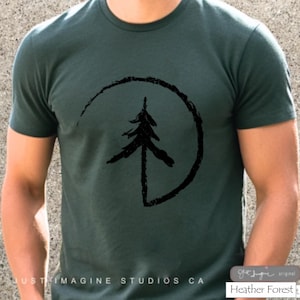 May include: Dark green t-shirt with a black tree graphic inside a circle. The text "JUST IMAGINE STUDIOS CA" is printed at the bottom. The shirt is labeled "Heather Forest" in the bottom right corner.