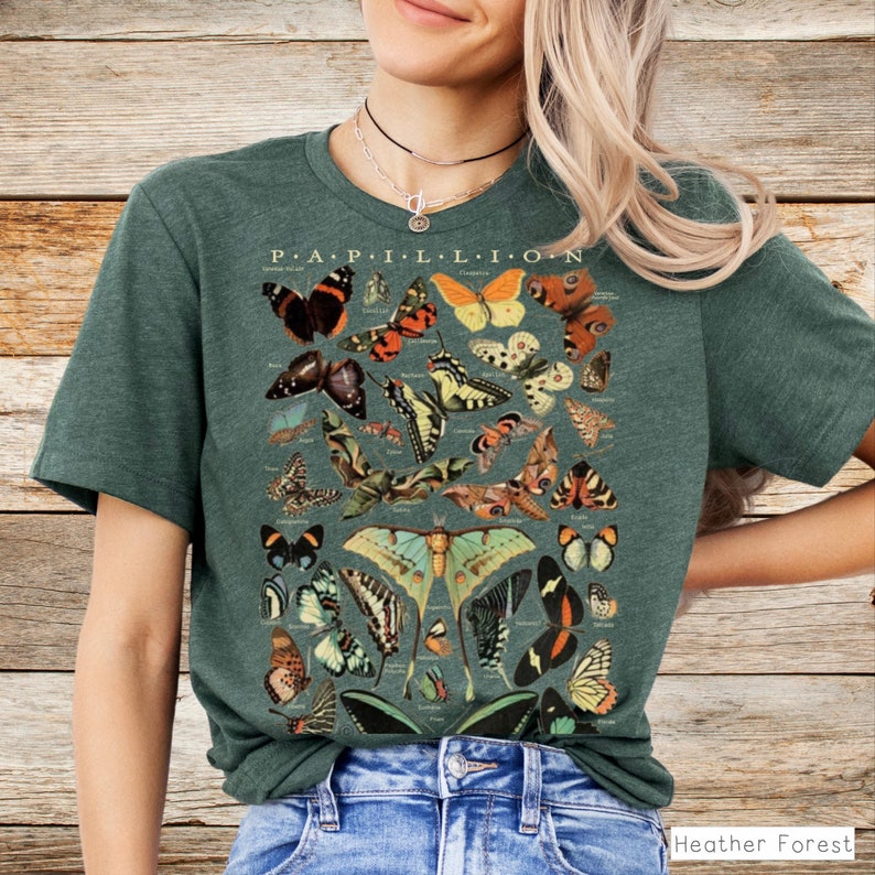 May include: A dark green t-shirt featuring a detailed illustration of various butterflies and moths. The word "PAPILLON" is printed at the top. The shirt is made of a soft material and has a classic crew neck.
