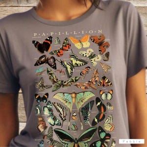 May include: Gray t-shirt featuring a detailed illustration of various butterflies, with the word "PAPILLON" across the top. The design includes butterflies in shades of orange, black, green, and blue.
