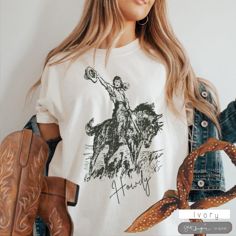 May include: A white t-shirt with a black and white illustration of a woman riding a horse. The text "Howdy" is written below the image.