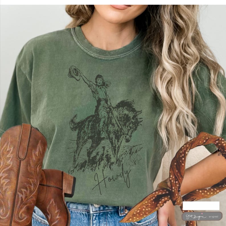 May include: A green t-shirt with a vintage illustration of a woman riding a horse. The text "Howdy" is printed below the image.