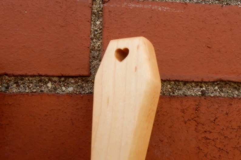 Puede incluir: Una cuchara de madera con un corte en forma de coraz&oacute;n. La cuchara es de color marr&oacute;n claro y tiene un acabado liso.