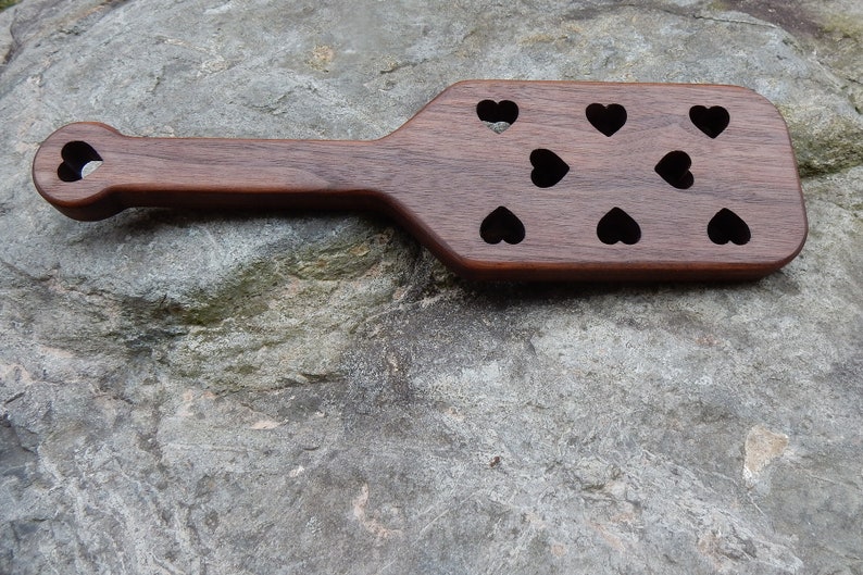 May include: A wooden paddle with a heart-shaped cutout at the top and multiple heart-shaped cutouts across the surface.