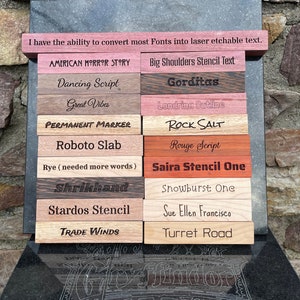 May include: A collection of wooden blocks with various fonts laser etched on them. The fonts include American Horror Story, Dancing Script, Great Vibes, Permanent Marker, Roboto Slab, Rye, Shrikhand, Stardos Stencil, Trade Winds, Big Shoulders Stencil Text, Gorditas, Londrina Outline, Rock Salt, Rouge Script, Saira Stencil One, Snowburst One, Sue Ellen Francisco, and Turret Road.