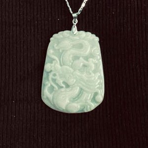 May include: A jade pendant necklace with a silver chain. The pendant is carved with a detailed design of a dragon.