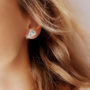 May include: A close-up of a woman's ear wearing a pair of small, triangular earrings with a white and black speckled pattern.