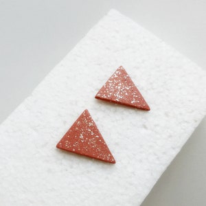 Puede incluir: Un par de pendientes en forma de triángulo hechos de terracota con un acabado moteado. Los pendientes son de color marrón rojizo con motas doradas.