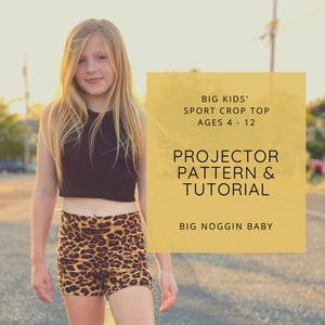 May include: A girl wearing a black crop top and leopard print shorts. The image includes text that reads "BIG KIDS' SPORT CROP TOP AGES 4 - 12 PROJECTOR PATTERN & TUTORIAL BIG NOGGIN BABY"