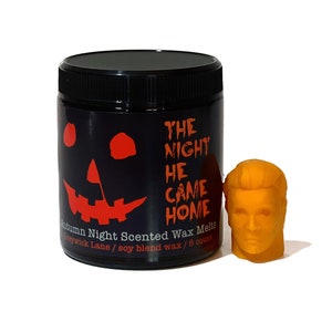 May include: A black jar of "Autumn Night Scented Wax Melts" with a jack-o'-lantern face and the text "The Night He Came Home" in orange. A small, orange wax melt shaped like a head is next to the jar.