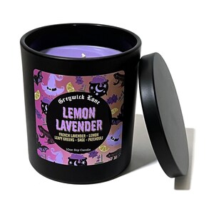 May include: A black candle jar with a matching lid, featuring a purple candle inside. The label reads "Lemon Lavender" with additional text. The label includes illustrations of witch hats, frogs, and moons. The candle is a 10oz soy candle.
