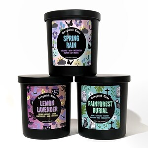 May include: Three black soy candles with labels. The top candle reads "Spring Rain" with bergamot, rain, and watermelon scents. The middle candle is "Lemon Lavender" with French lavender and lemon scents. The bottom candle is "Rainforest Burial".