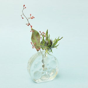 May include: A clear glass vase with a textured surface, filled with a small arrangement of dried flowers and greenery. The vase is round and has a wide opening.