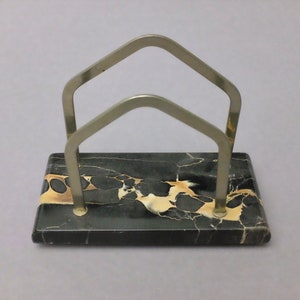 May include: A black marble letter holder with a silver metal frame. The marble has a swirling pattern of black, white, and gold.