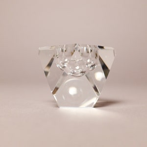 May include: A clear glass candle holder with a geometric design. The holder has a round opening in the center and a flat base.