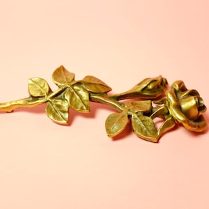 May include: A gold-toned metal rose brooch with detailed leaves and a stem.