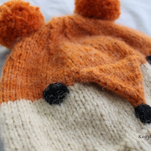 May include: A knitted fox hat with orange and white fur, black felt eyes and nose, and two orange pom-poms on top.