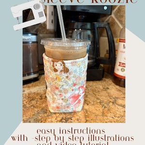 May include: A floral fabric cup sleeve, or koozie, featuring Disney princesses Belle and Ariel, surrounds a clear plastic cup with a straw. The image includes text that reads "cup/can/jar sleeve-koozie" and "easy instructions with step by step illustrations and video tutorial."