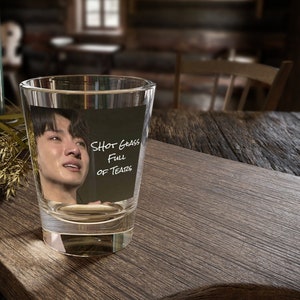 May include: A clear glass shot glass with a picture of a person crying inside. The text "Shot Glass Full Of Tears" is written on the glass.