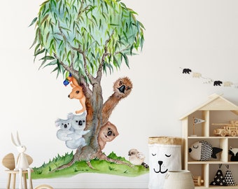 Op de afbeelding: Een aquarel-illustratie van een treurwilg met een kangoeroe, een emoe en drie koala's die achter de stam vandaan kijken. De boom is omringd door groen gras en er vliegen vogels boven.