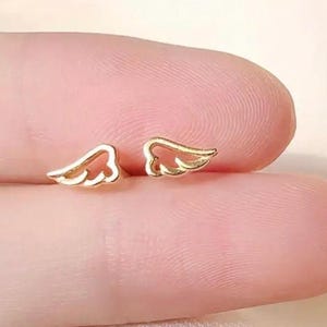 May include: A pair of gold-colored angel wing earrings. The wings are delicate and have a cutout design.