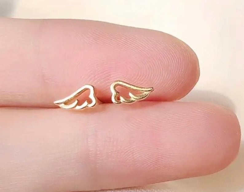 May include: A pair of gold-colored angel wing earrings. The wings are delicate and have a cutout design.