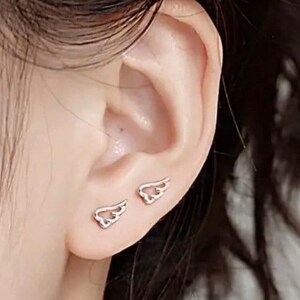 May include: A pair of silver wing-shaped earrings. The earrings are small and delicate, and they are worn in the lobes of the ears.