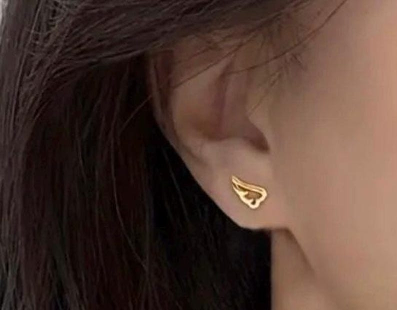 May include: A pair of gold wing-shaped earrings. The earrings are small and delicate, and they are worn in the wearer's earlobes.