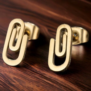 May include: A pair of gold-toned paperclip shaped stud earrings. The earrings are made of metal and have a simple, modern design.