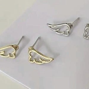 May include: A pair of gold and silver angel wing stud earrings. The earrings are simple and delicate, with a minimalist design.
