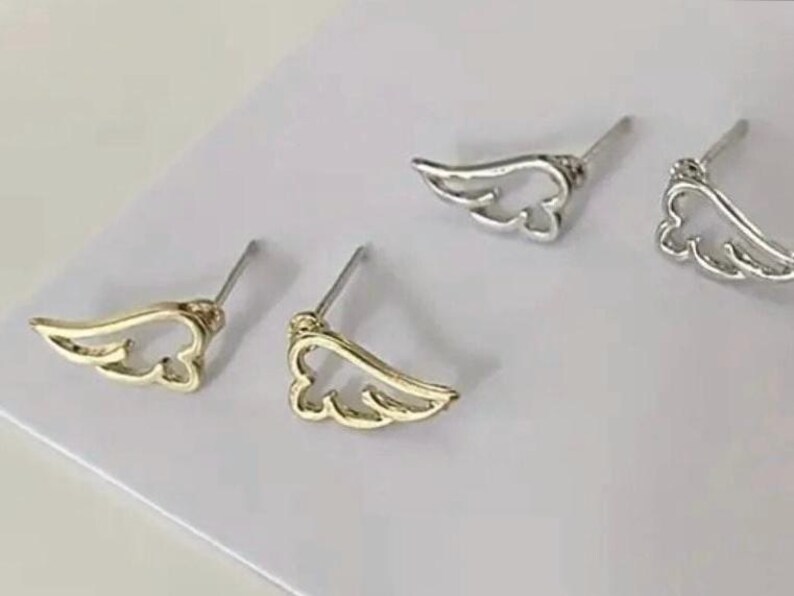 May include: A pair of gold and silver angel wing stud earrings. The earrings are simple and delicate, with a minimalist design.