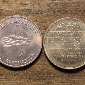Puede incluir: Dos monedas conmemorativas de New Hampshire. Una moneda presenta un contorno del estado con "Mt. Washington" inscrito debajo. La otra moneda tiene un águila, el texto "The Granite State" y detalles sobre la ratificación de la Constitución.