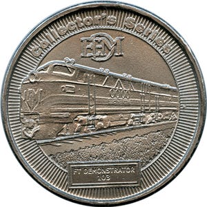 May include: A silver coin from the Collector's Series featuring a detailed depiction of a train locomotive. The coin has the text "Collector's Series" and "FT Demonstrator 103". The train is labeled "3000 Electromotive".