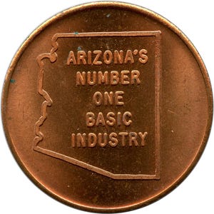 May include: A copper-colored coin featuring the outline of Arizona and the text "ARIZONA'S NUMBER ONE BASIC INDUSTRY." The coin has a circular shape with a slightly worn appearance, and the text is embossed.