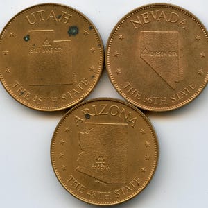 Puede incluir: Tres monedas conmemorativas de color bronce. Una moneda presenta el estado de Utah, con el texto "SALT LAKE CITY" y "THE 45TH STATE". Otra moneda muestra Nevada, con "CARSON CITY" y "THE 36TH STATE". La tercera muestra Arizona, con "PHOENIX" y "THE 48TH STATE".