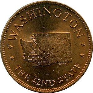 May include: A bronze-colored coin featuring the outline of Washington state. The coin is inscribed with "WASHINGTON" at the top and "THE 42ND STATE" at the bottom. The city of Olympia is also visible.