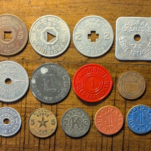 May include: A selection of vintage sales tax tokens and emergency relief tokens in various shapes, sizes, and colours. The tokens feature text such as "Sales Tax," "Emergency Relief Fund," and state names like "Missouri" and "Colorado."