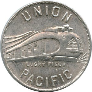 May include: A silver coin featuring a detailed depiction of a streamlined train. The coin is inscribed with "UNION PACIFIC" and "LUCKY PIECE". The coin has a textured edge and a vintage aesthetic.