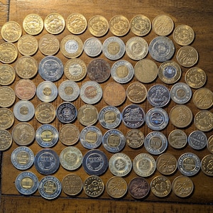 May include: A collection of over 70 round, silver and gold tokens with various designs and text. The tokens are arranged in a circular pattern on a wooden surface.