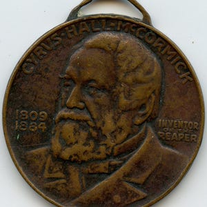 May include: A bronze-colored medal featuring a portrait of Cyrus Hall McCormick, with the text "CYRUS HALL MCCORMICK" at the top. The years "1809" and "1884" are inscribed, along with "INVENTOR OF THE REAPER".