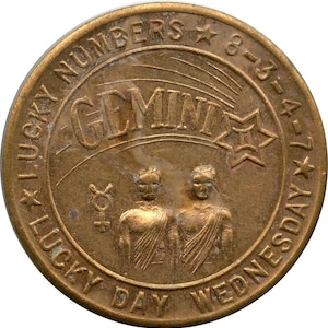 May include: A bronze-colored Gemini token with the words "Lucky Numbers" and "Lucky Day Wednesday" around the edge. The center features the word "Gemini", two figures, and a shooting star design.