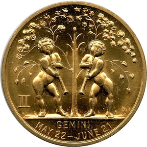 May include: A gold-colored coin featuring two cherubic figures playing flutes, with a tree between them. The coin is inscribed with "GEMINI" and "MAY 22 - JUNE 21". The Gemini symbol is also present.