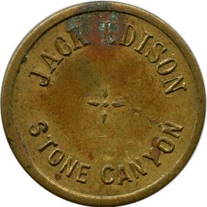 Op de afbeelding: Een ronde, antieke messing token met de woorden "JACK EDISON STONE CANYON" in reliëf langs de rand. Een vierpuntig sterontwerp staat in het midden. De token heeft een versleten, verouderde uitstraling.