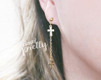 Op de afbeelding: Gouden oorhangers met twee kleine kruisbedels die aan een delicate ketting hangen.